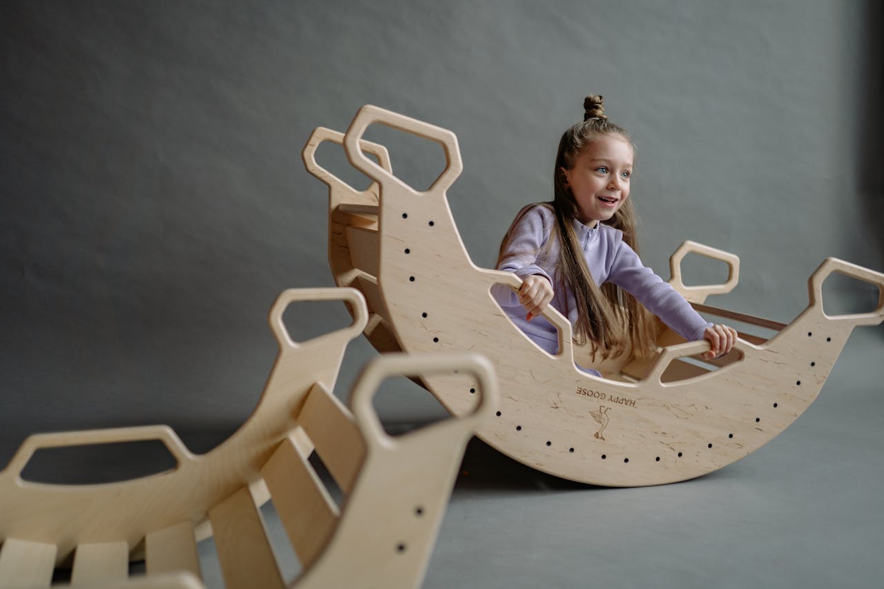 A joyful child plays on a wooden rocking toy in an indoor playground setting.